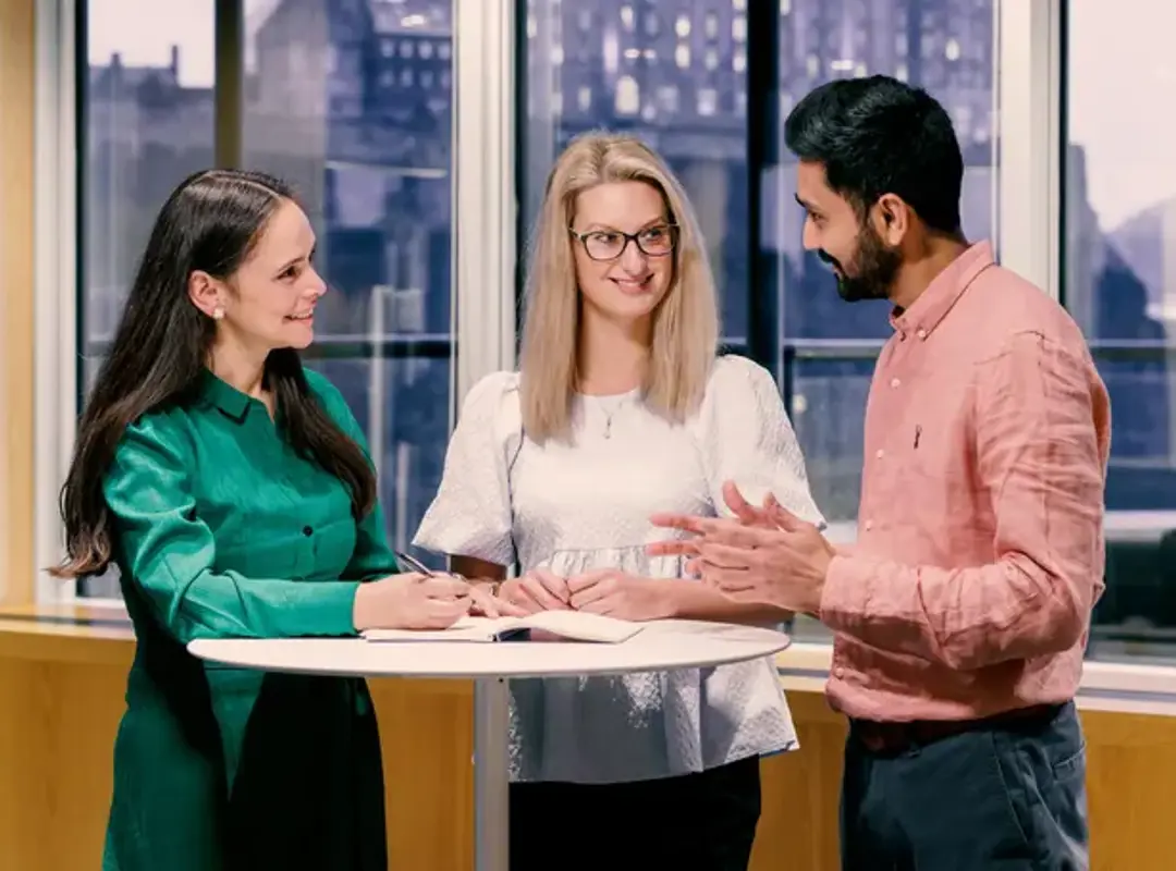 Three people standing at a table beside window