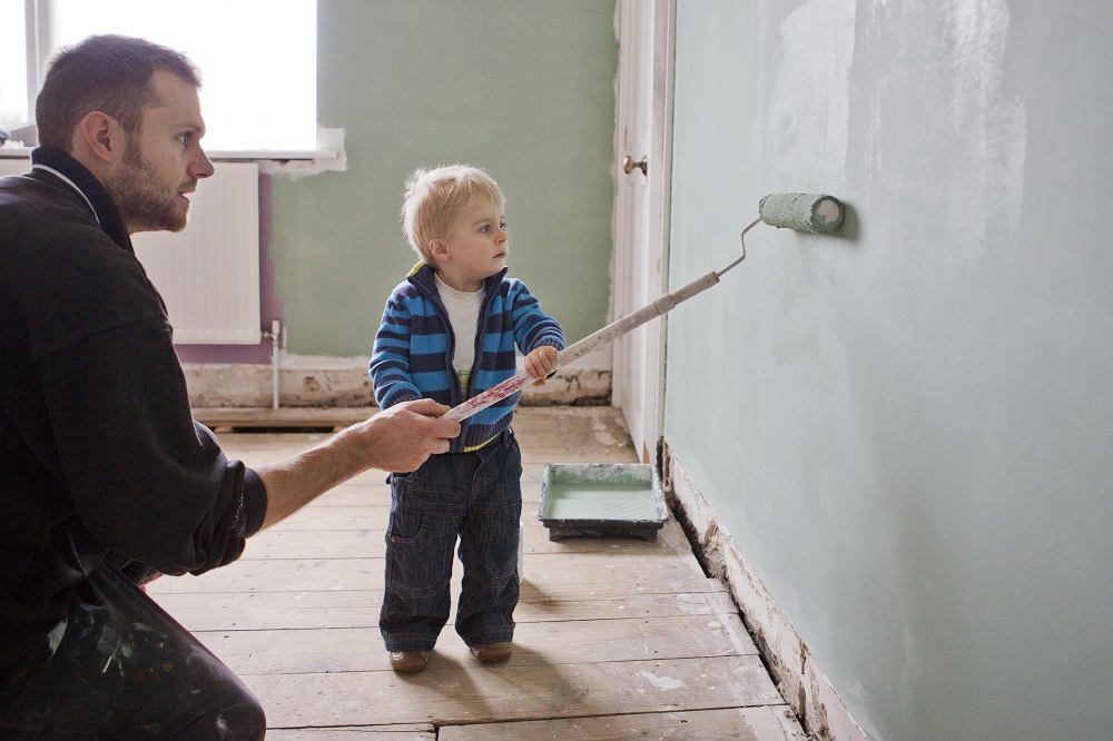 Parent And Child Painting A Wall With A Roller Brush