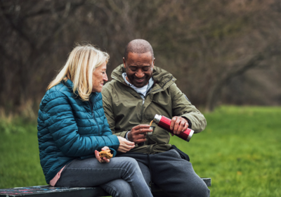 People Having A Hot Drink On A Park Bench