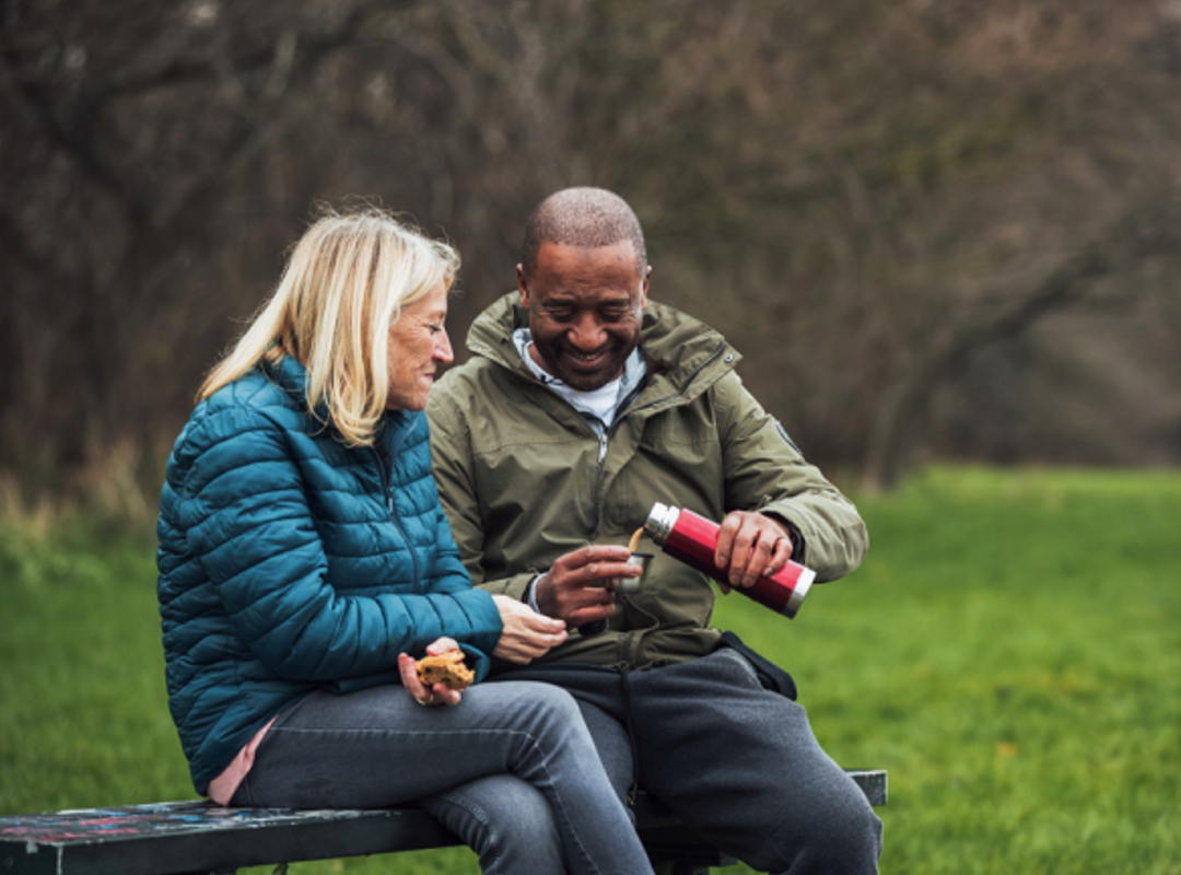 People Having A Hot Drink On A Park Bench